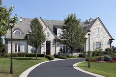 a large house with two driveways and trees in the front yard on a sunny day