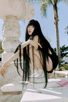 a woman with long black hair sitting on a bench