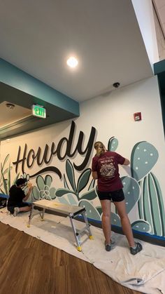 a woman painting a mural on the side of a building in front of a wooden floor