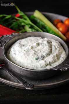 a metal bowl filled with white dip surrounded by vegetables