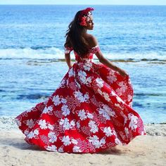 a woman in a red and white dress walking on the beach near the ocean,