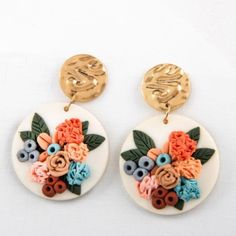 a pair of earrings with flowers and leaves painted on the back of them, sitting on a white surface