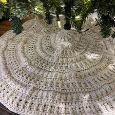 a crocheted christmas tree skirt is shown under a pine tree in the sunlight