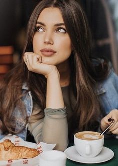 a woman sitting at a table with a cup of coffee and croissant in front of her