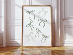 an art print with green bows on it in front of a white wall and wooden floor