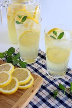 two glasses of lemonade on a table with sliced lemons and mint sprigs