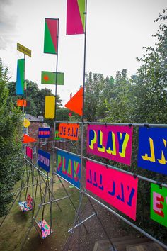 many colorful signs are hanging on a metal fence