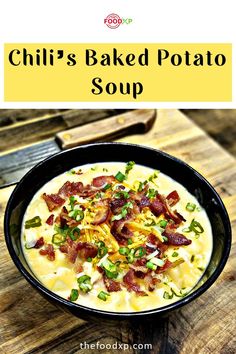 a bowl of soup with bacon, cheese and green onions in it on a wooden table