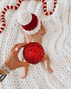 a person holding a red ornament on top of a white knitted blanket