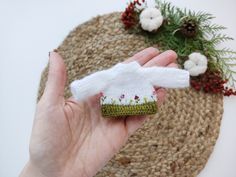 a hand holding a small knitted hat on top of a rug next to flowers