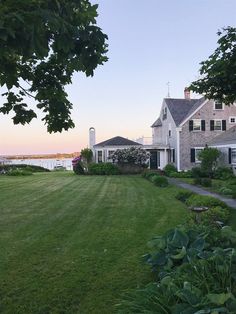 a large house sitting on the side of a lush green field next to a body of water