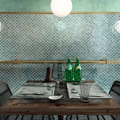 the table is set for two with empty glasses and bottles on it in front of a mosaic tile wall