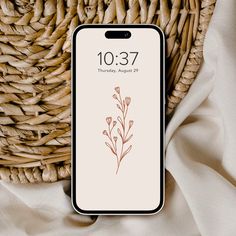 an iphone with the date on it sitting next to a wicker basket and white cloth