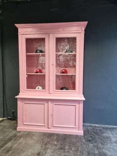 a pink china cabinet sitting on top of a hard wood floor next to a blue wall