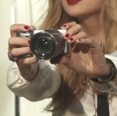 a woman taking a selfie in front of a mirror with her camera and red nail polish