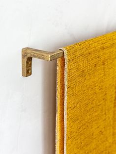 a yellow towel hanging on the wall next to a metal hook that is attached to it