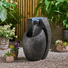 a water fountain in the middle of a gravel area with potted plants around it