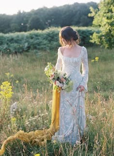 a woman is standing in the grass holding a bouquet