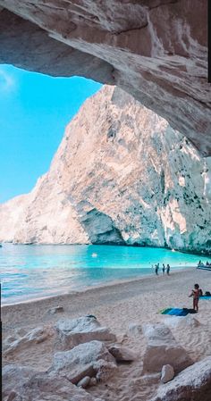 people are on the beach under an arch near the water and mountains in the background