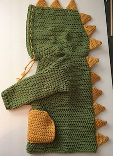 a crocheted green and yellow dragon costume next to some knitting needles on a white surface