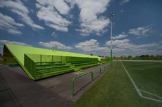 an empty soccer field with green benches and lights on the sidelines under a cloudy blue sky