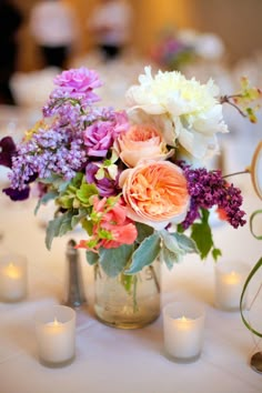 a vase filled with lots of flowers sitting on top of a table next to candles