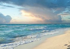 footprints in the sand on a beach with waves coming towards the shore and clouds overhead