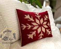 a red and white pillow sitting on top of a bed next to a green plant