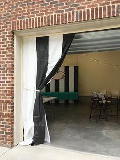 an open garage door with black and white drapes on the outside, next to tables and chairs