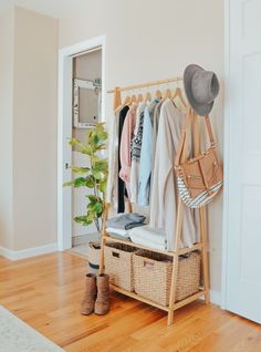 an open closet with clothes and shoes hanging on the rack, next to a potted plant