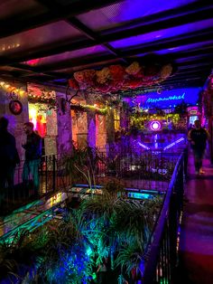 people are walking around in an indoor area with plants and decorations on the walls, along with colorful lights