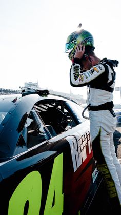 a man talking on a cell phone next to a racing car in a parking lot