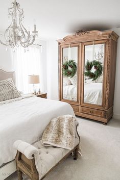 a bedroom with a white bed and wooden armoires in front of a chandelier