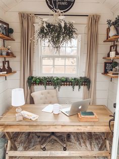 a wooden table with a laptop on top of it in front of a window filled with potted plants