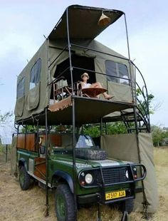 a green truck parked in the grass with a tent on top of it's roof