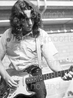 a man with long hair playing an electric guitar in front of a stadium bleachers