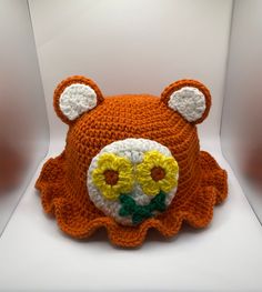 a crocheted teddy bear hat with yellow flowers on it's face and ears