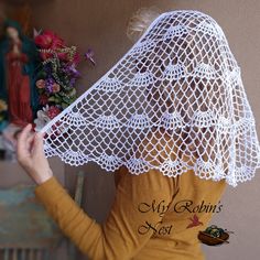 a woman wearing a white crochet veil over her head with flowers in the background