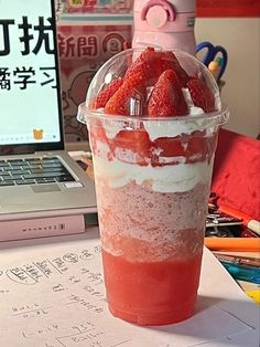 a cup filled with strawberries sitting on top of a table next to a laptop