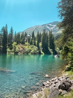 a lake surrounded by trees and rocks in the middle of a mountain range with clear blue water