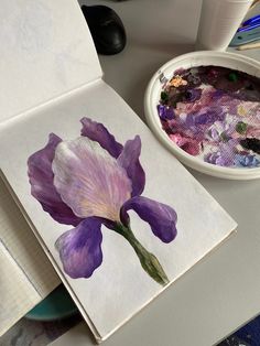 a purple flower sitting on top of a white paper next to a bowl of paint