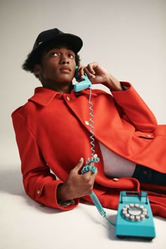 a woman sitting on the floor while talking on a phone and holding a blue telephone