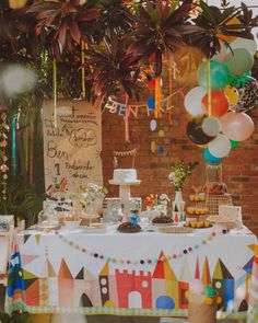 a table topped with cake and balloons next to a brick wall covered in greenery