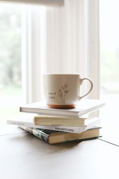 a stack of books sitting on top of a table next to a cup and saucer