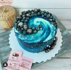 there is a blue cake with white frosting and berries on the top, next to a wicker basket