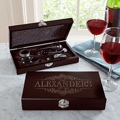 two glasses of red wine are sitting on a table next to an open box that says,'alexandders '