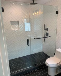 a white toilet sitting in a bathroom next to a walk in glass shower stall with black tile on the floor