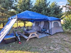 a tent set up in the middle of a field with picnic tables and chairs under it