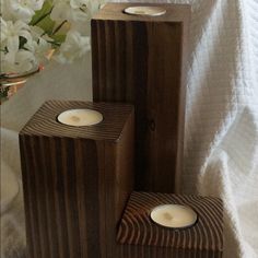 three wooden candles sitting on top of a white bed next to flowers and a vase