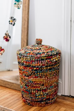 a multicolored basket sitting on the floor in front of a mirror with beads hanging from it